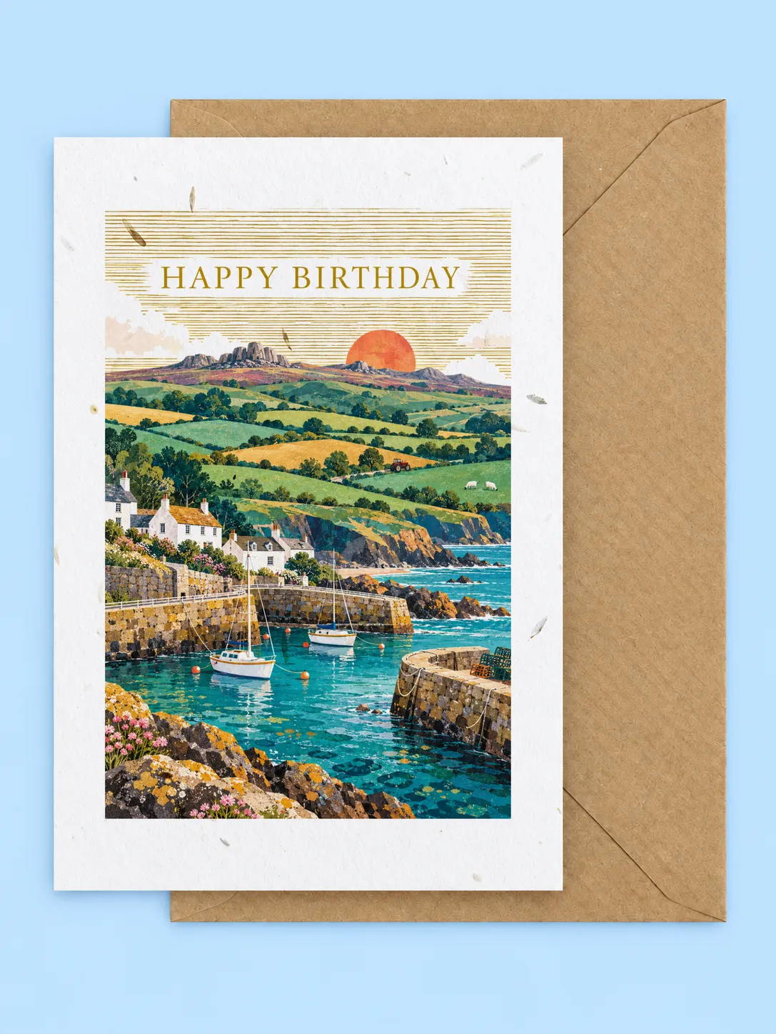 Cornish harbour with fishing boats, rolling green fields and a setting sun, Happy Birthday plantable birthday card with a kraft envelope on a pale blue background