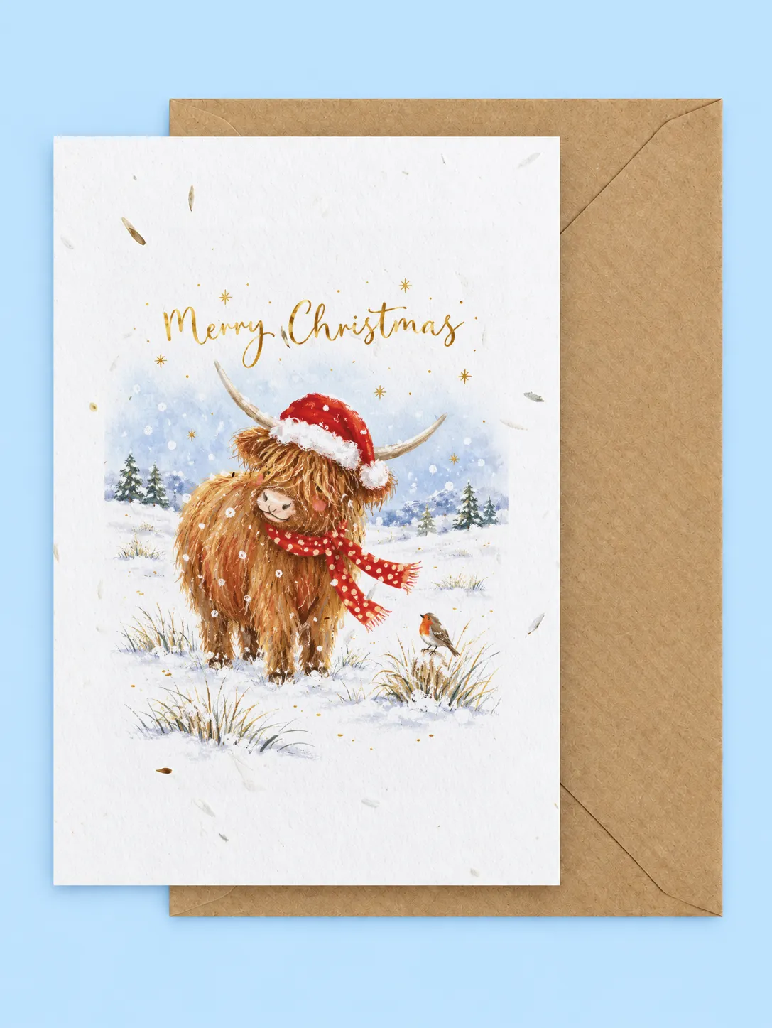 Highland cow in a Santa hat and red scarf with a robin in a snowy field, plantable Christmas card with a kraft envelope on a pale blue background
