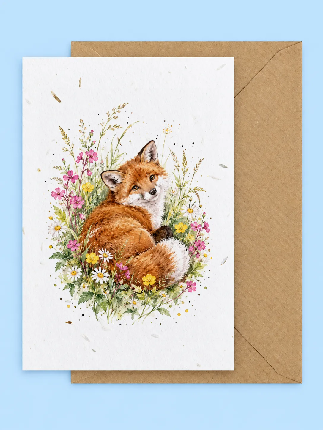 Red fox curled up among pink and yellow wildflowers and grasses, seed paper greetings card with a kraft envelope on a pale blue background