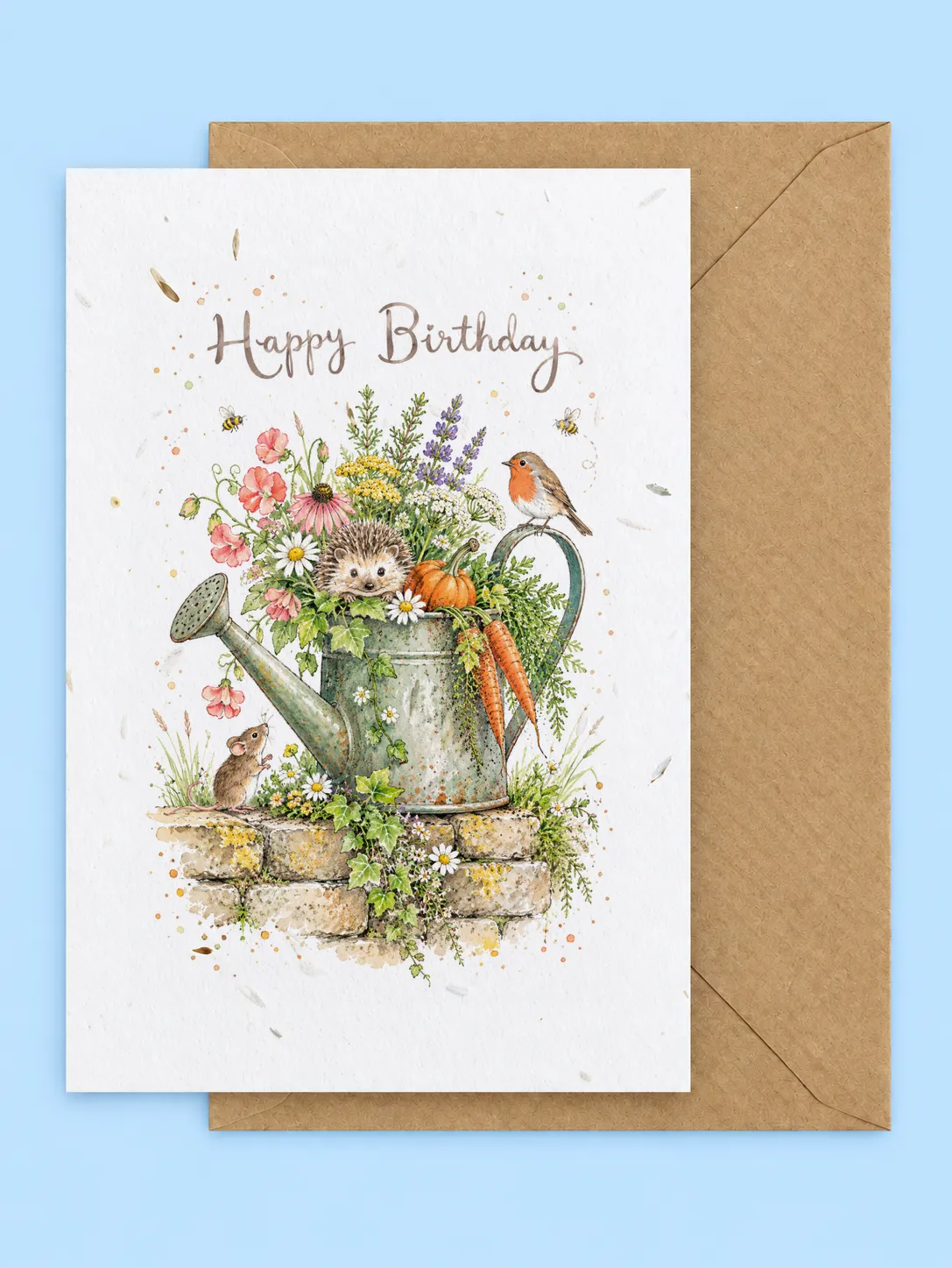 Hedgehog in a watering can full of wildflowers with a robin and mouse on a stone wall, plantable birthday card with a kraft envelope on a pale blue background