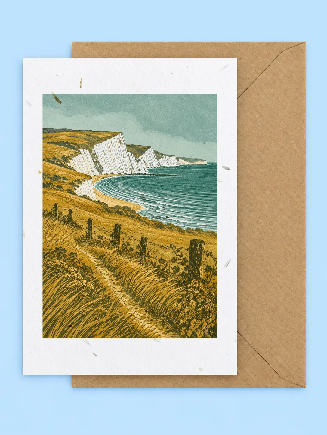 White chalk cliffs and a coastal footpath above a sandy bay, Jurassic Coast plantable greetings card with a kraft envelope on a pale blue background