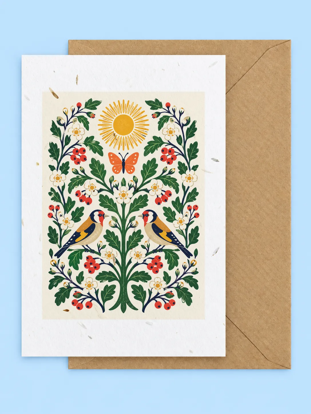 Symmetrical folk art design of goldfinches, butterflies, red flowers and a sun, seed paper greetings card with a kraft envelope on a pale blue background