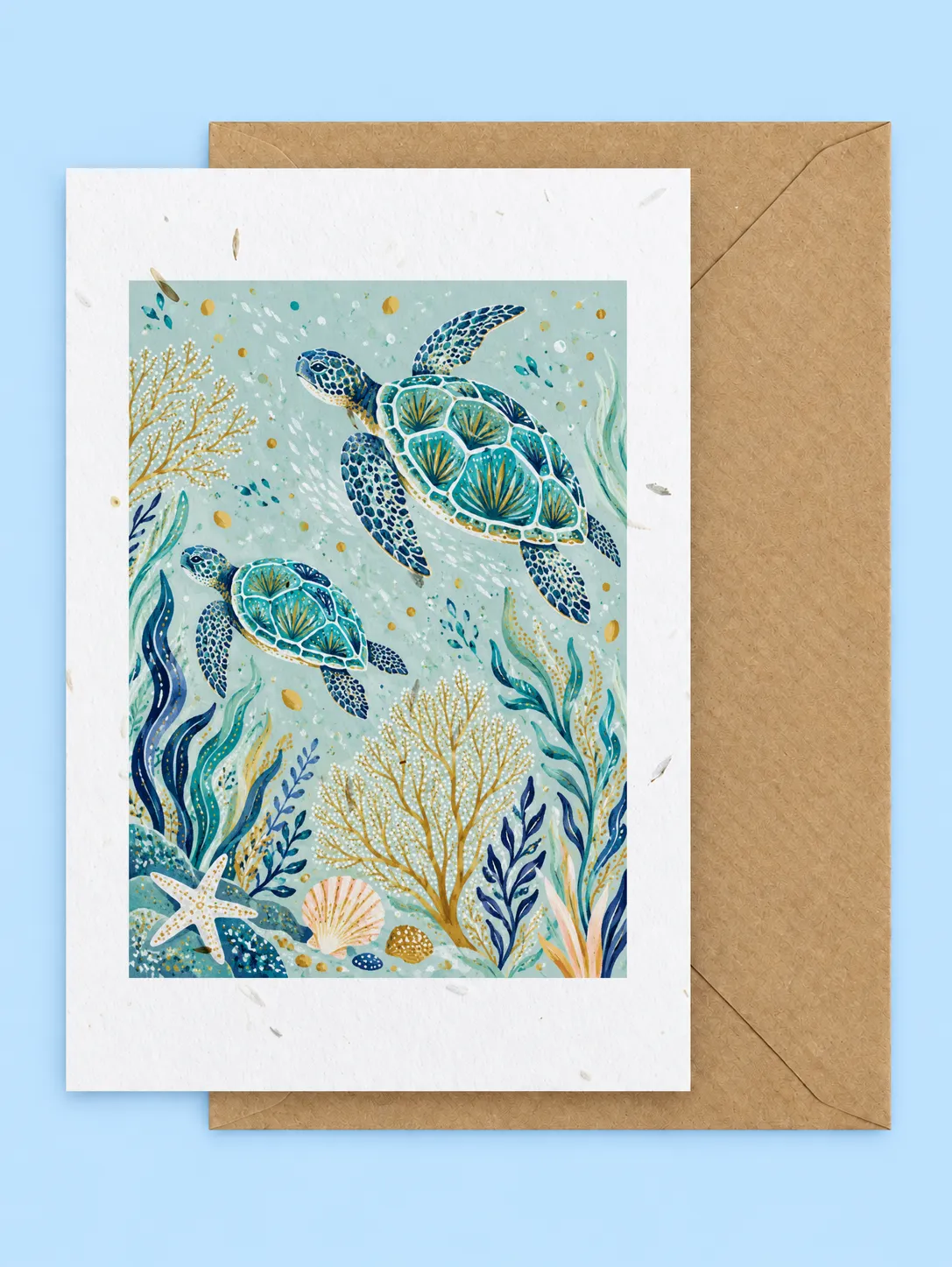 Two sea turtles swimming among coral, seaweed and shells in turquoise water, seed-filled greetings card with a kraft envelope on a pale blue background