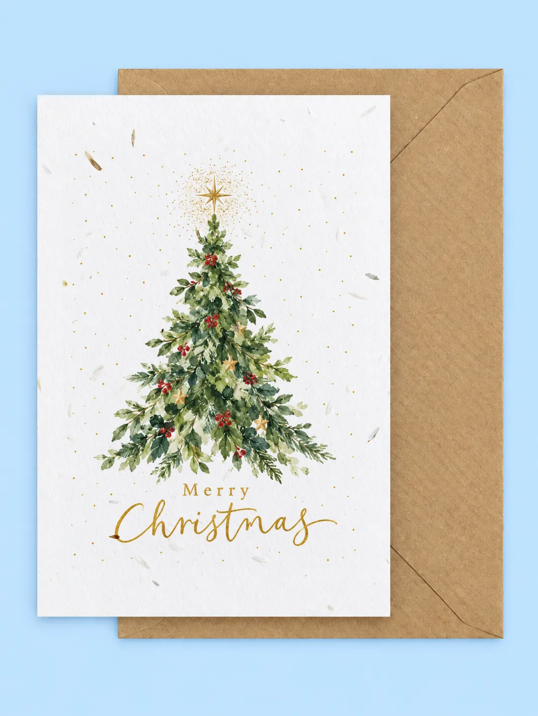 Decorated Christmas tree with red baubles and a gold star above Merry Christmas script, seed-filled Christmas card with a kraft envelope on a pale blue background