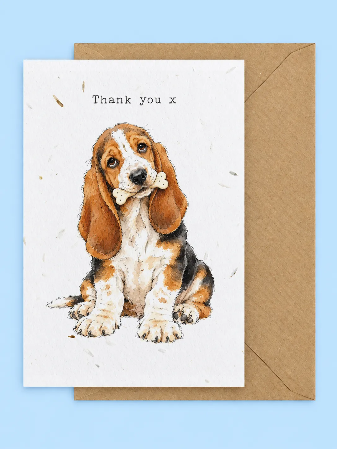 Basset hound puppy holding a bone in its mouth with Thank you x lettering, plantable thank you card with a kraft envelope on a pale blue background